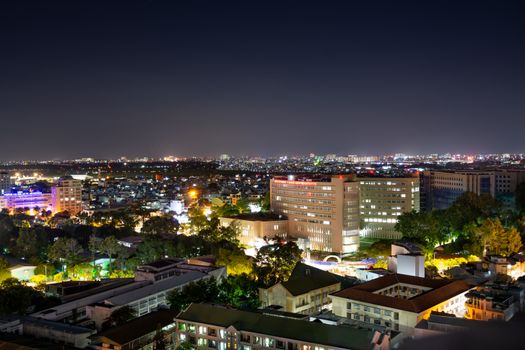 Aerial shot of a bustling cityscape at night with brightly lit buildings and urban sprawl.