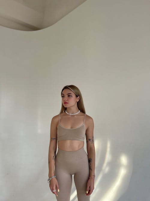 A Woman in Beige Activewear Standing Near White Wall while Looking Afar