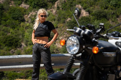 A Woman in Black Shirt and Pants Standing Beside the Motorcycle with Her Hands on Her Waist