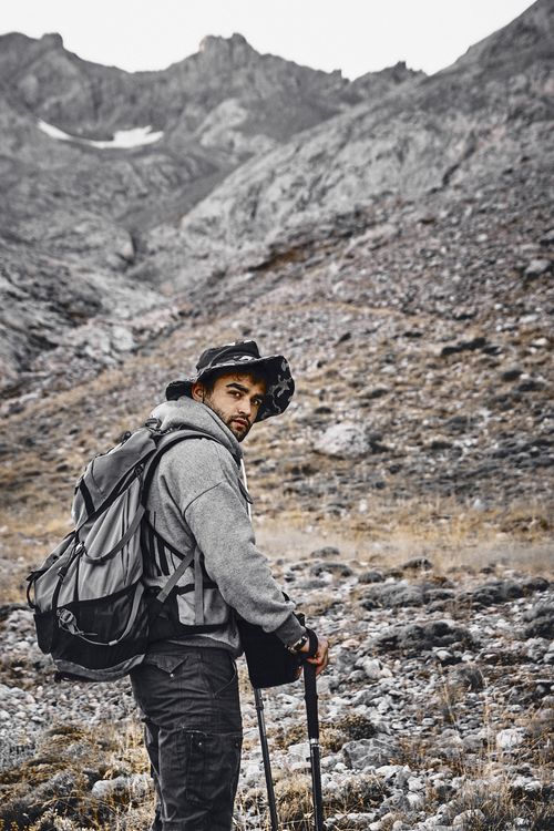 Free Man hiking in rugged rocky mountain terrain, carrying a backpack and wearing a hat. Stock Photo