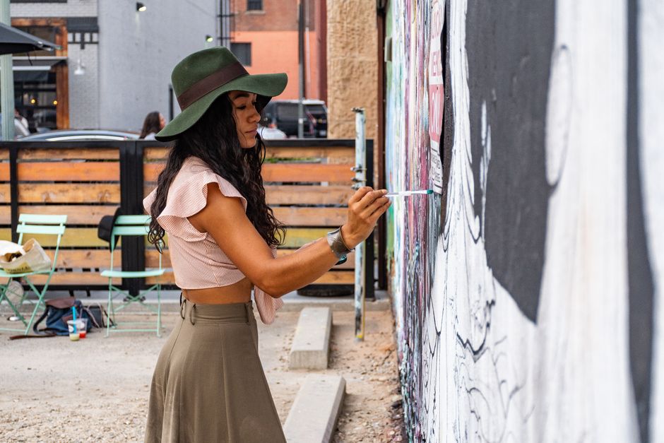 Woman artist painting a mural on an urban street wall with vibrant creativity.