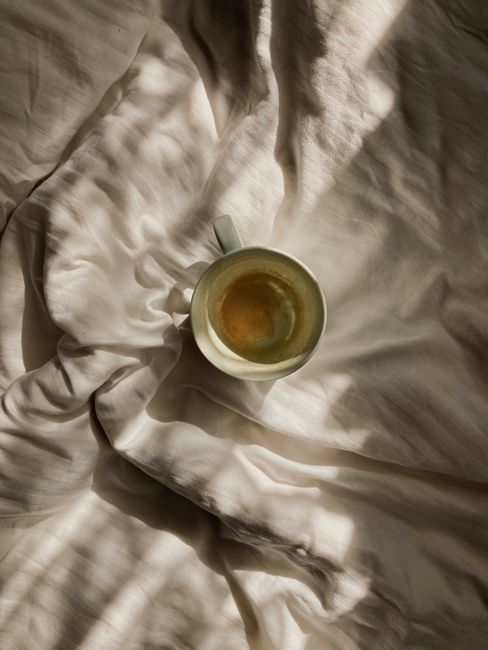 Warm cup of coffee resting on sunlit bed linens creating a cozy morning vibe.