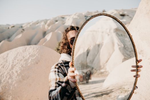 Person in plaid jacket holds mirror reflecting a desert landscape, creating an artistic visual effect.