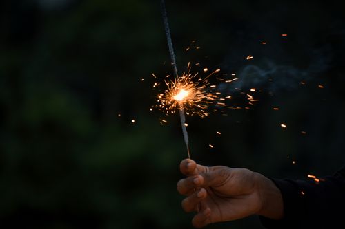 Free Hand holding a lit sparkler, creating a radiant display of sparks against a dark background. Stock Photo