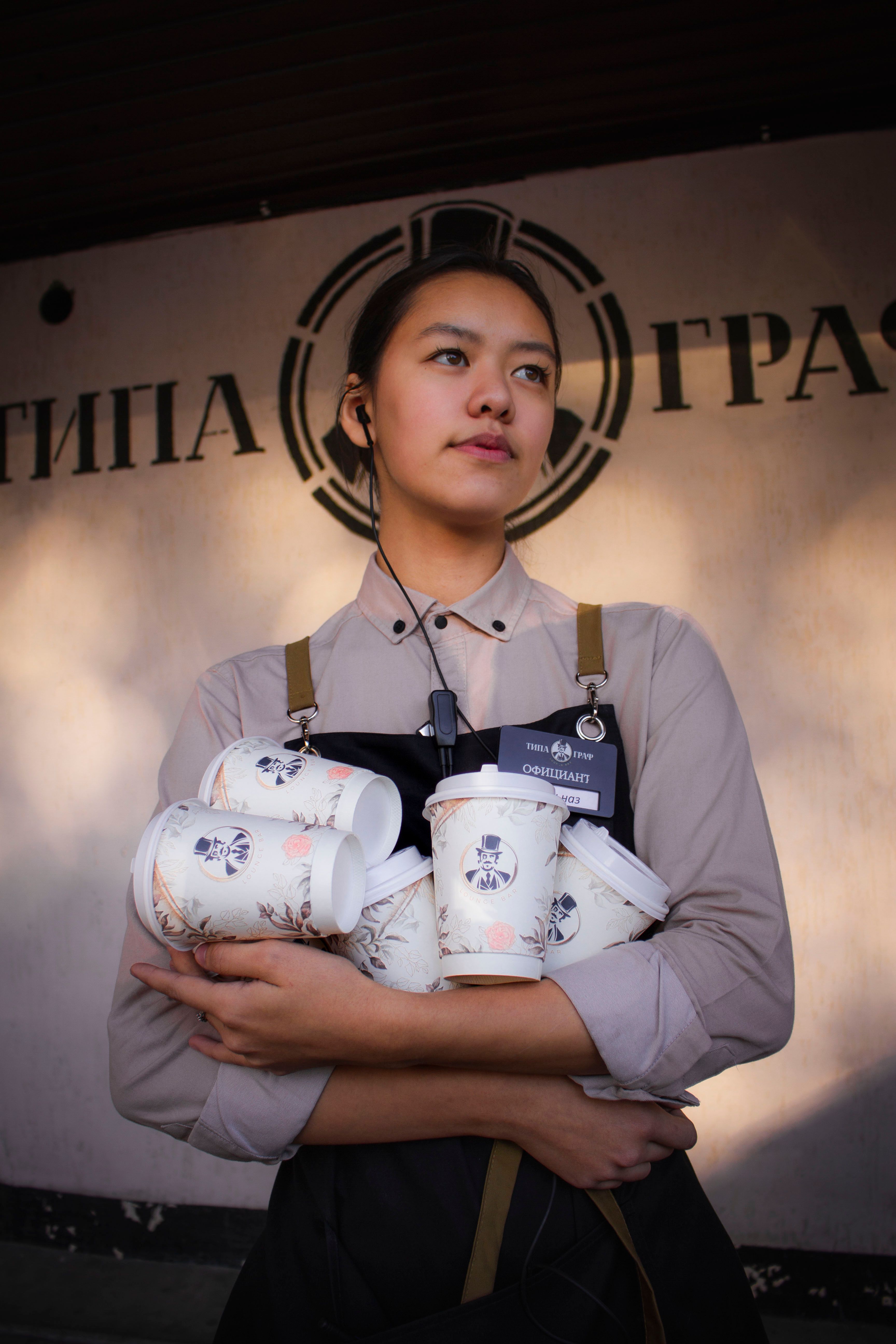 Young woman barista holding multiple disposable coffee cups in a cafe.