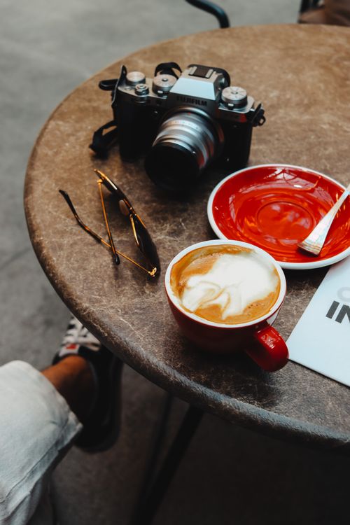 Free A tabletop scene with cappuccino, camera, and sunglasses, creating a cozy café vibe. Stock Photo