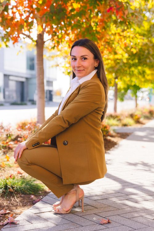 Free Professional woman in brown suit smiling while kneeling on sidewalk in fall. Stock Photo