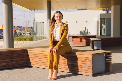 A Woman in Yellow Blazer and Pants Sitting on a Wooden Bench