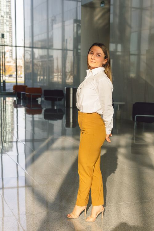 Free Woman in white shirt and yellow pants in a sunlit modern office building. Stock Photo
