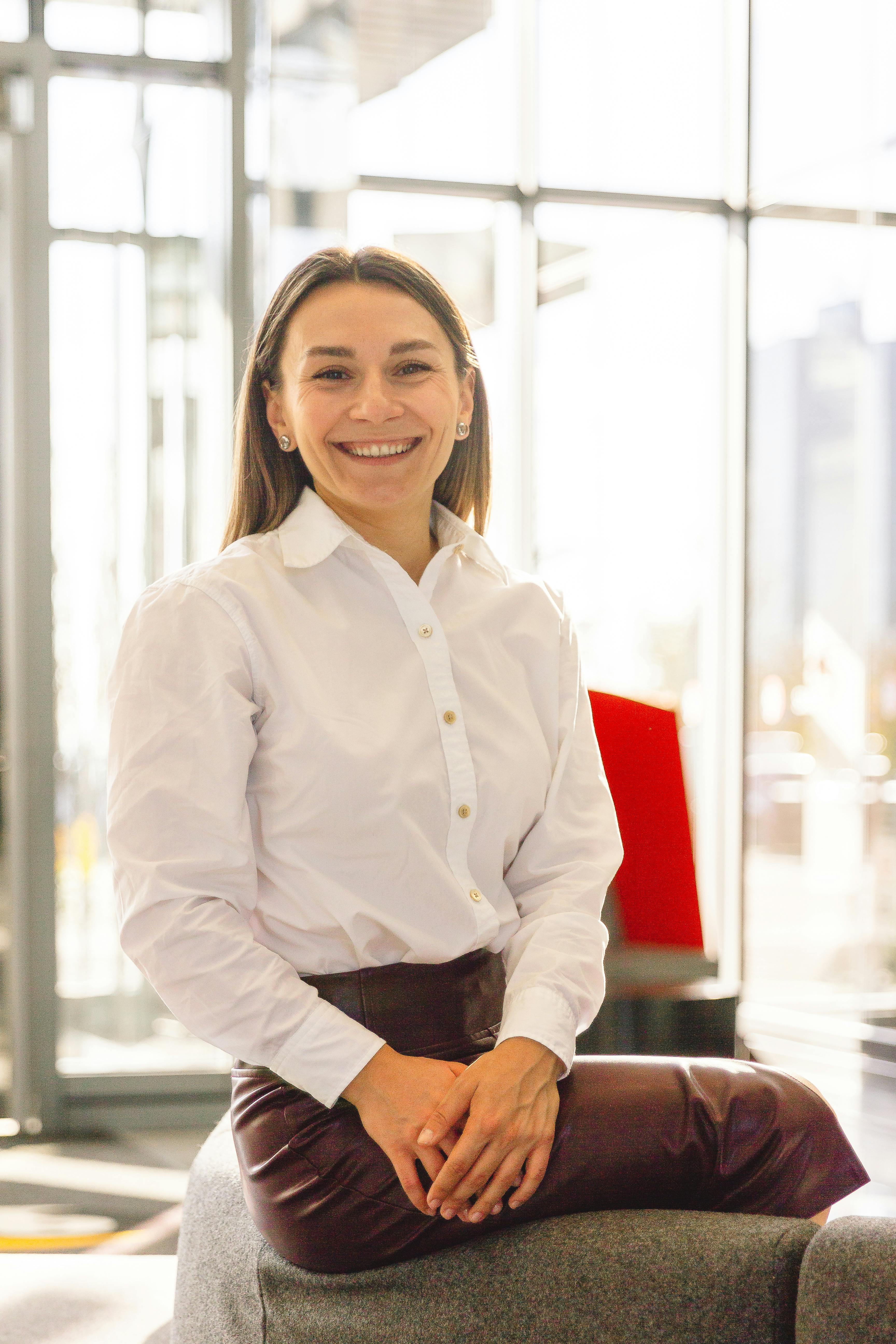 Professional woman in white blouse smiling while sitting in a modern office.