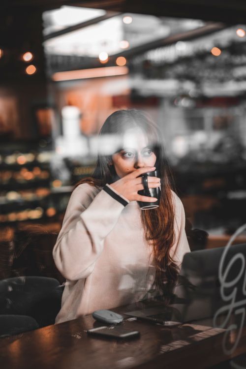 Free Young woman sipping coffee at a cafe table with warm ambient lighting. Stock Photo