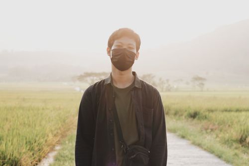 Free A young adult wearing a mask stands in a sunlit field in Yogyakarta, Indonesia. Stock Photo