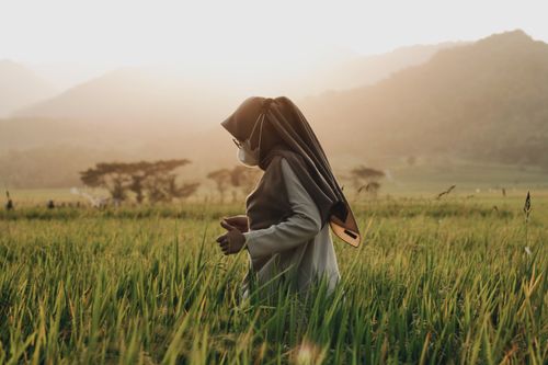 Free A woman wearing a hijab and face mask in a sunlit field in Yogyakarta, Indonesia, symbolizing new normal. Stock Photo