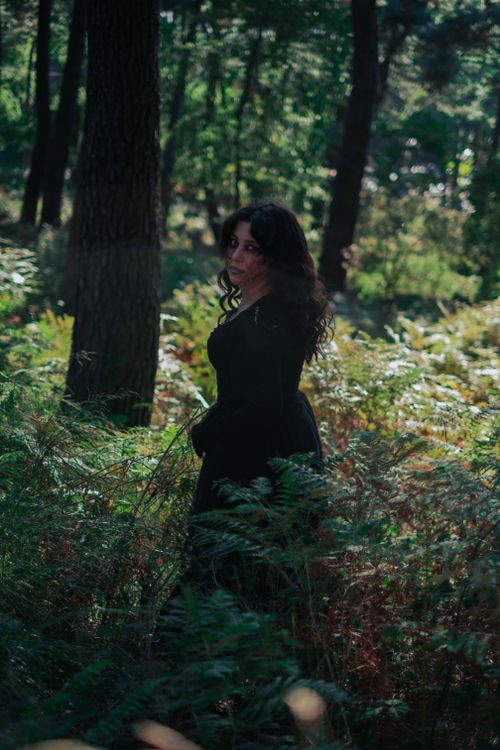 Free A woman in a black dress stands amidst lush greenery in a serene forest. Stock Photo