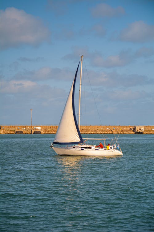 A White Sail Boat on a Body of Water Under Blue Sky
