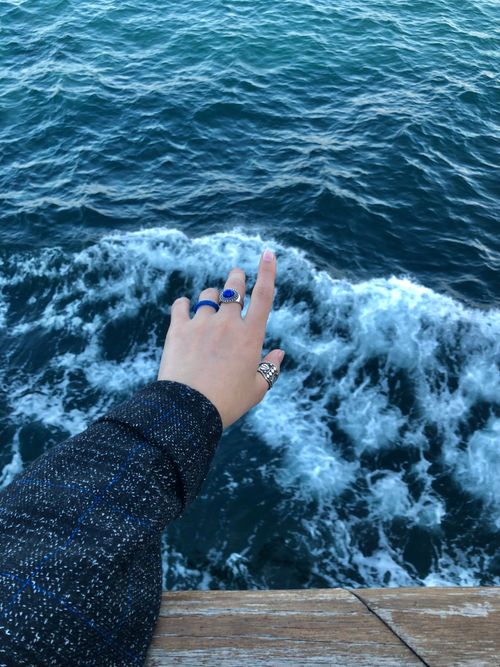 Free A hand adorned with rings extends over the edge of a pier, reaching toward the ocean waves below. Stock Photo