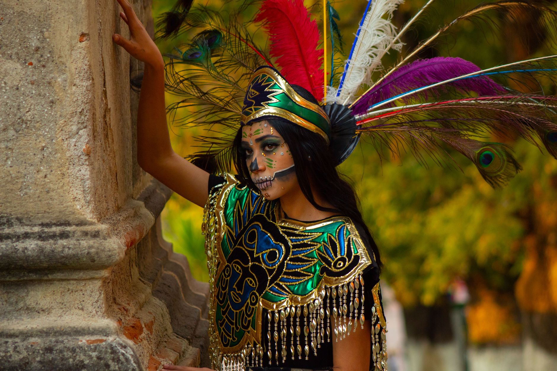 Young woman in colorful traditional attire and feathered headdress, outdoors.
