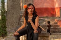 Woman in traditional Catrina makeup for Día de los Muertos with a vibrant orange flower.