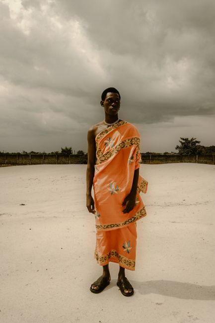 A man in traditional clothing stands confidently in a sandy outdoor setting in Lagos, Nigeria.
