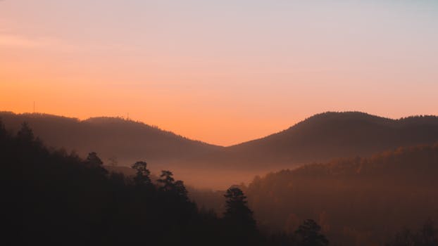 Peaceful mountain landscape at sunrise with soft orange hues and misty valleys.