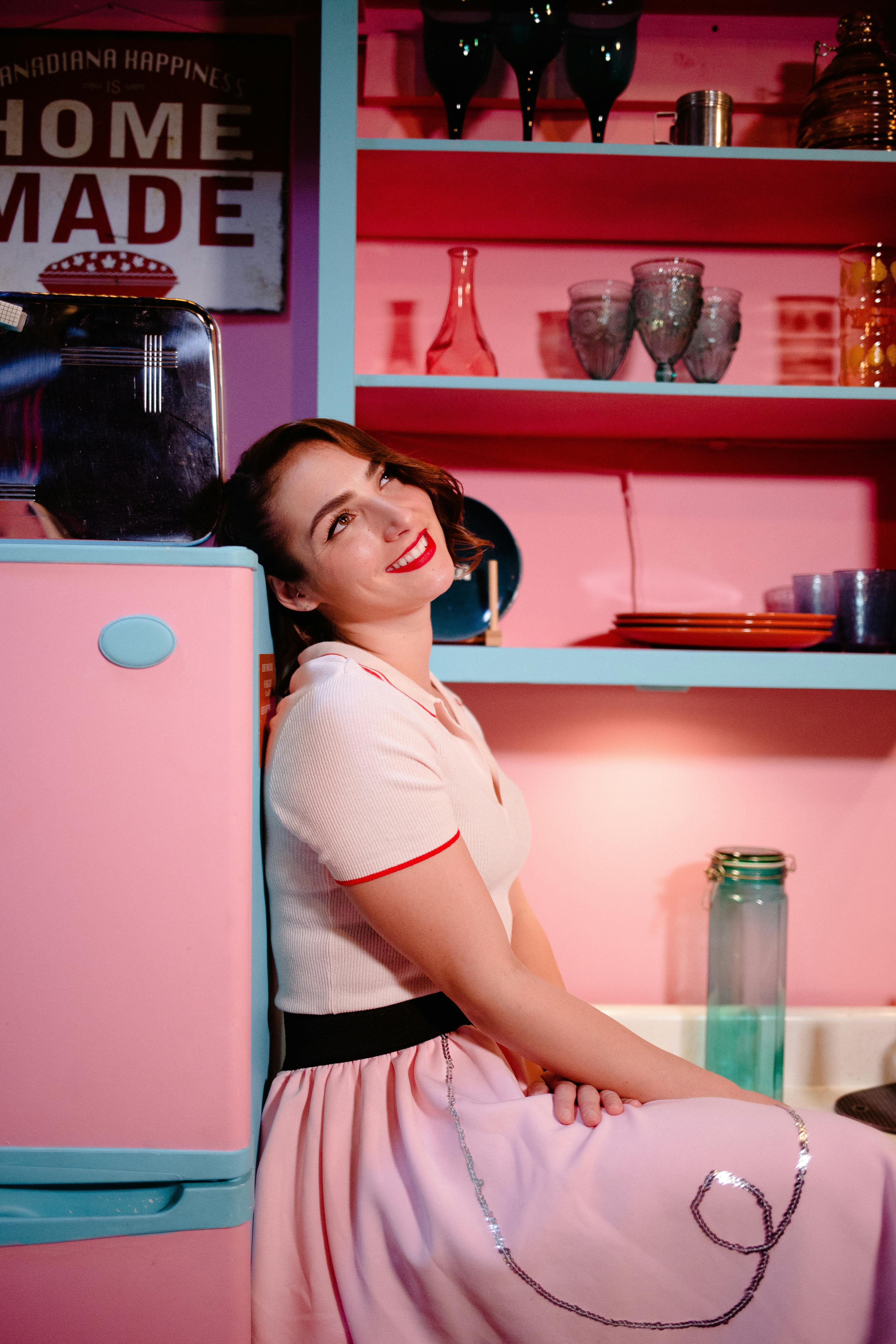 A woman poses with a smile in a retro kitchen setting with vibrant colors.