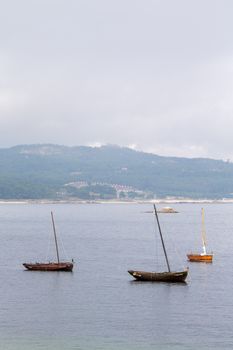 Three traditional sailboats anchored on serene waters in El Grove, Spain.