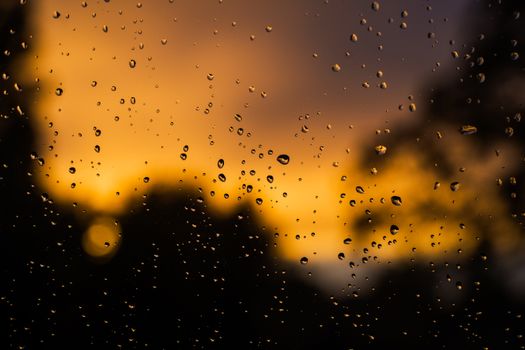 Raindrops on glass with a dramatic, vibrant sunset background.