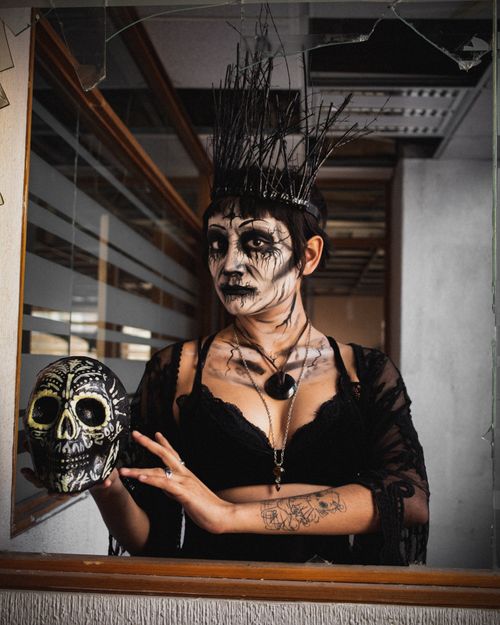 Free Woman in dark attire with skull makeup holds a decorative skull in a dramatic portrait indoors. Stock Photo