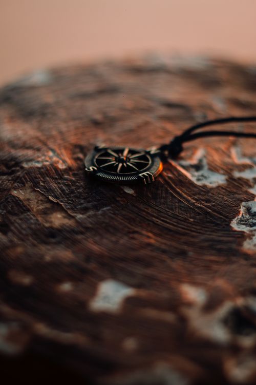 Free Close-up of a compass pendant on a textured wooden surface with warm lighting. Stock Photo