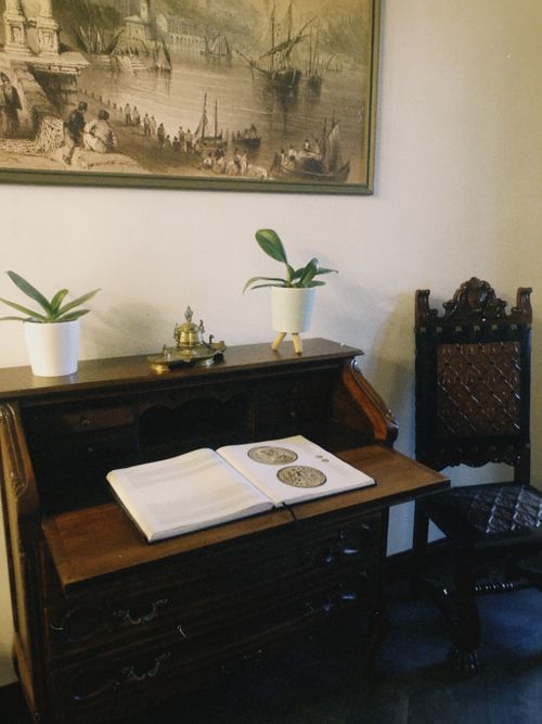 Free Antique wooden desk setup with open book, framed painting, and vintage chair. Stock Photo