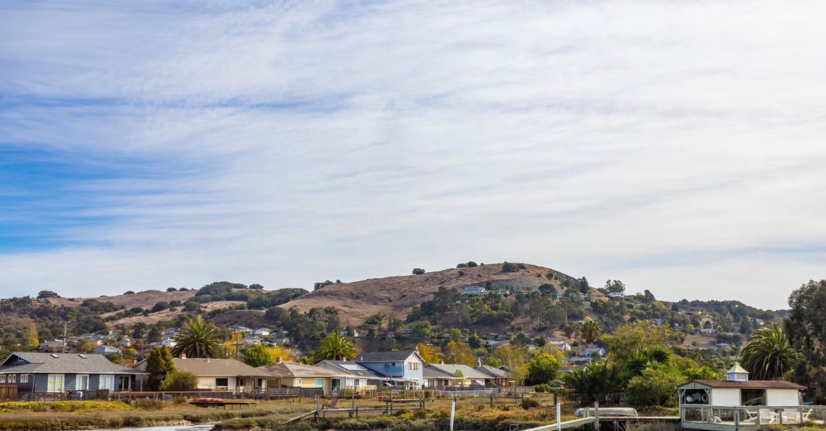 Charming waterfront town with hills, houses, and a tranquil river under a blue sky.