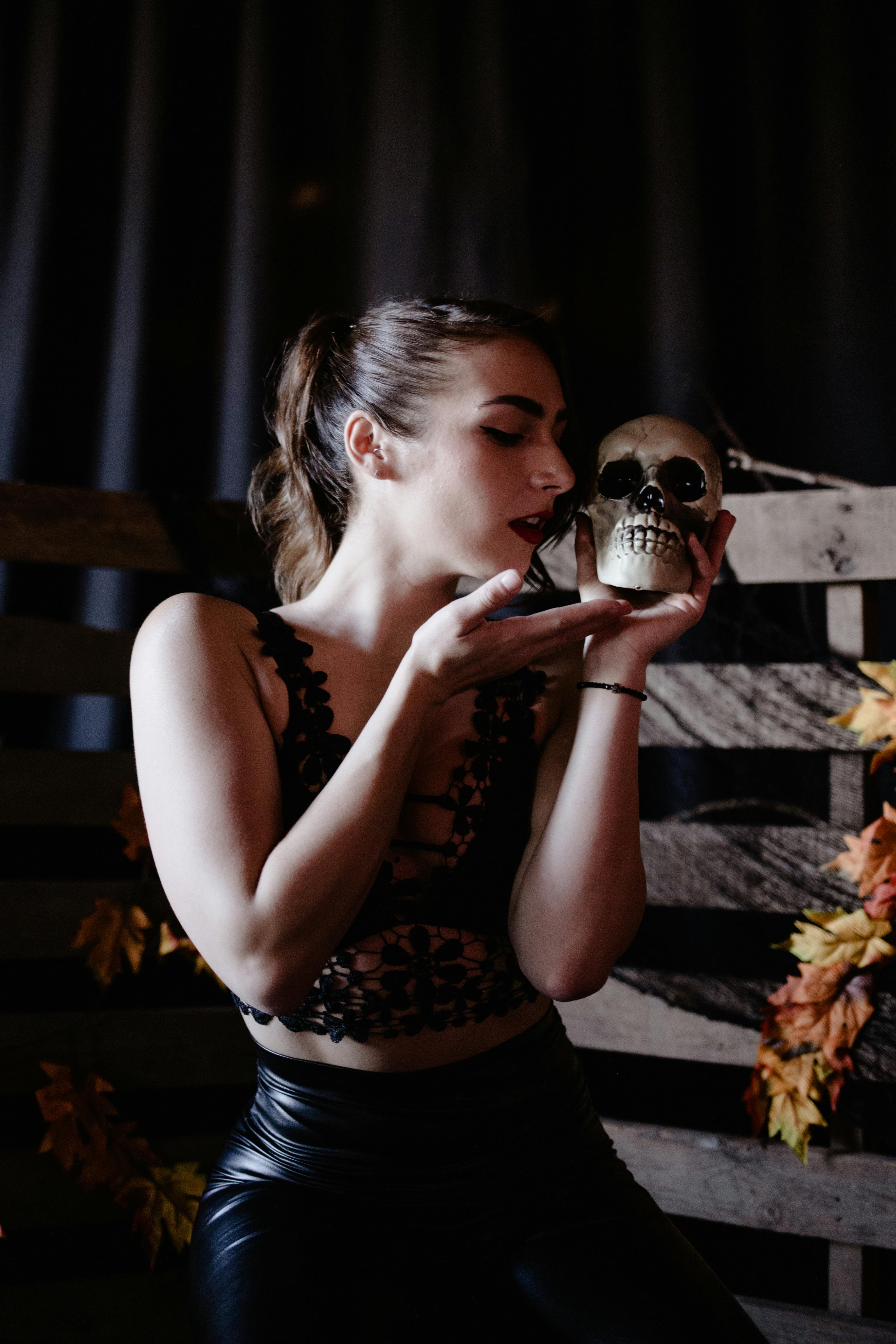 Free A woman in dark attire poses with a skull, evoking a mysterious and eerie atmosphere. Stock Photo
