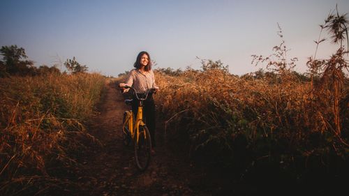 Free A young woman walks with a bicycle on a rural dirt road in Nagpur during sunrise. Stock Photo
