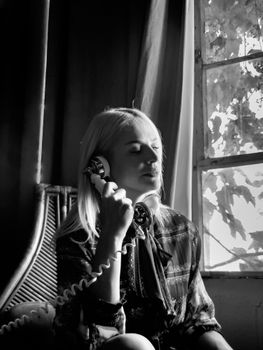 Elegant black and white portrait of a woman using a retro phone by a window, evoking nostalgia.