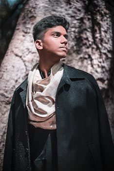 一位时尚男模特在户外戴着围巾、穿着深色外套摆姿势，展现现代风格