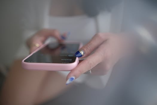 A woman with manicured nails using a smartphone indoors in West Java, Indonesia.