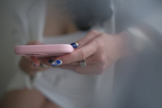 A close-up view of a woman with manicured nails using a smartphone indoors.