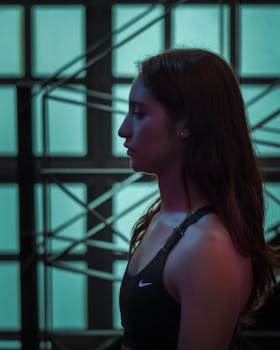 Side profile of a young woman in a dimly lit indoor setting, wearing activewear.
