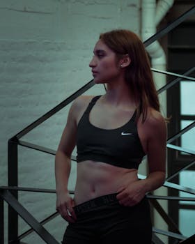 A young woman in activewear stands confidently on an industrial staircase, showcasing fitness fashion.