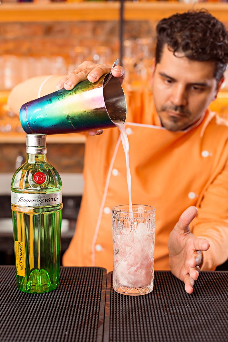 Bartender pouring gin into a cocktail glass with ice