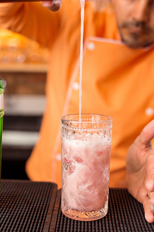 Person Pouring Pink Liquid on Clear Drinking Glass Glass