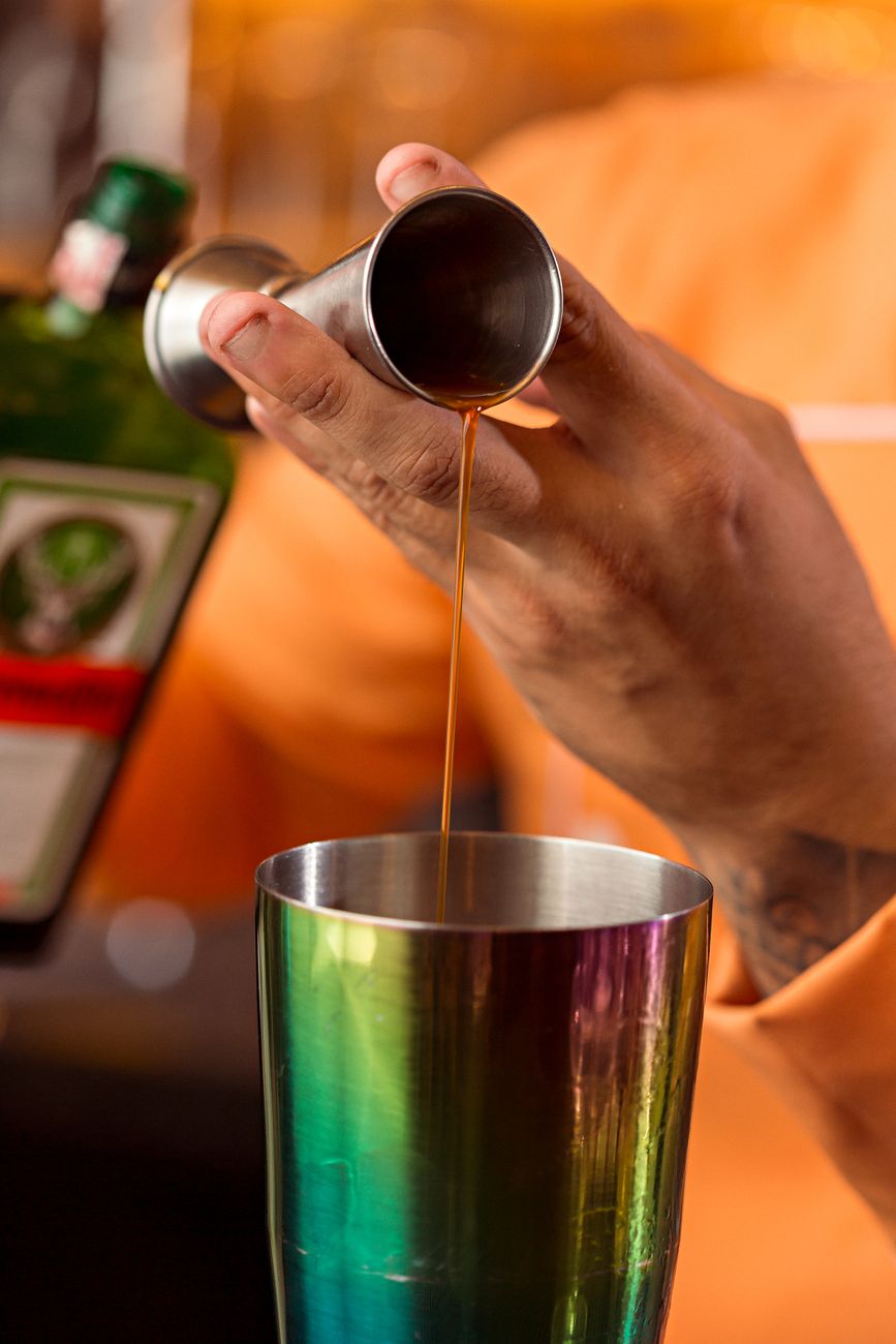 Bartender pouring a cocktail into a shaker behind a busy bar