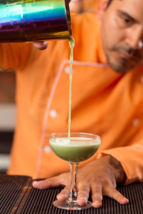 Free A focused bartender expertly pours a vibrant green cocktail, showcasing mixology skills. Stock Photo