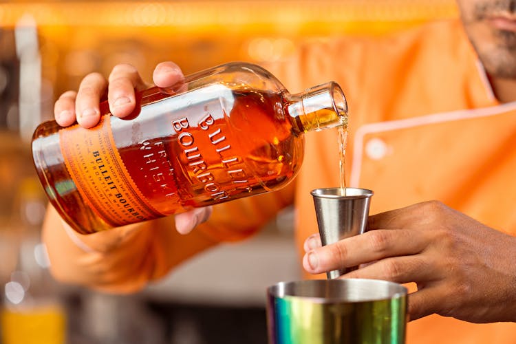 Person Holding A Bottle Of Liquor And Stainless Jigger