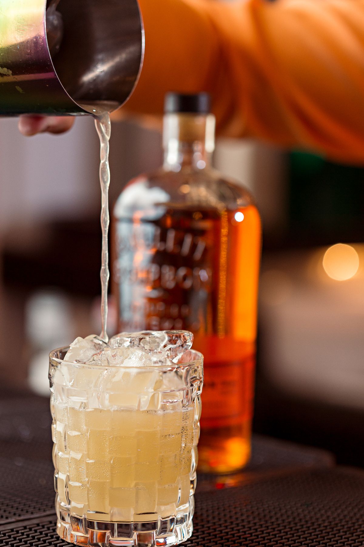 Bartender straining a craft cocktail into a chilled glass at the bar