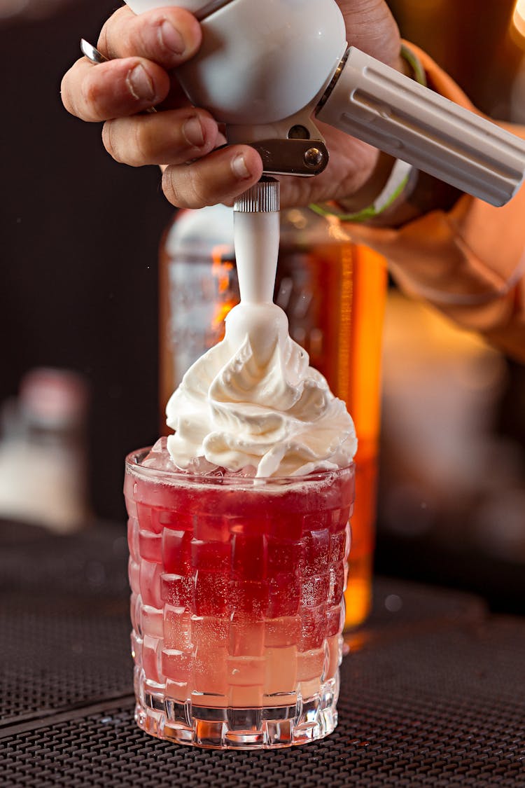 Hand Adding Whipped Cream On Top Of Cocktail