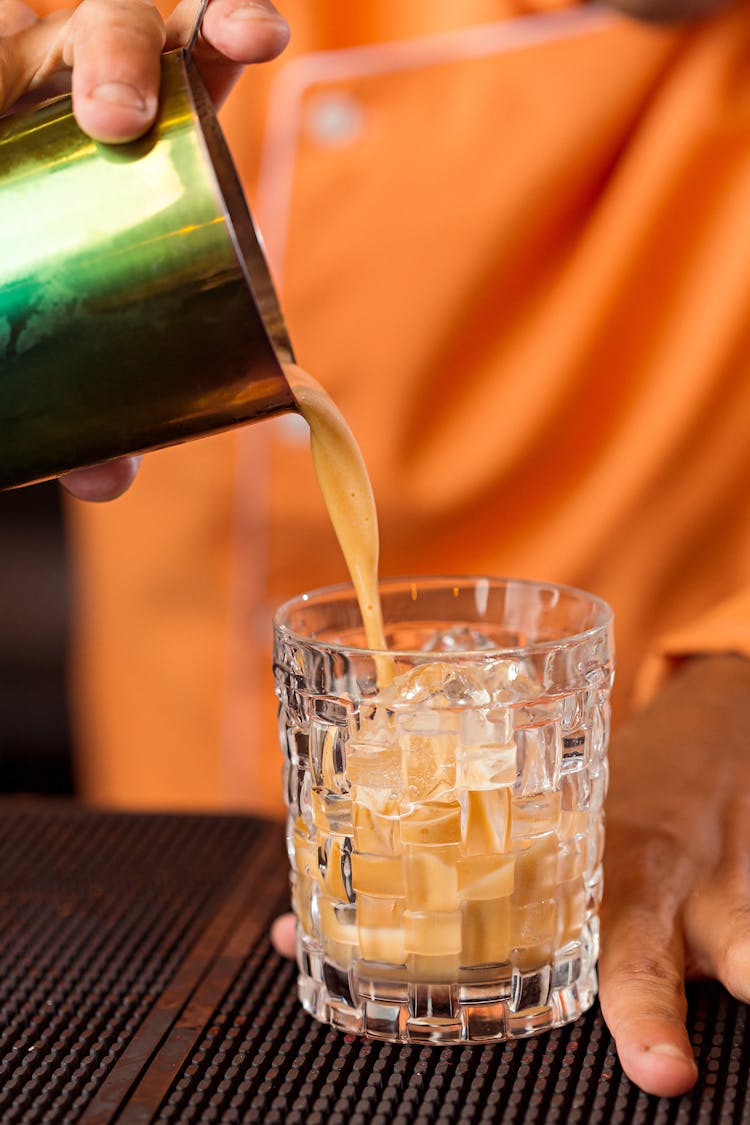 Person Pouring Orange Liquid In Clear Drinking Glass