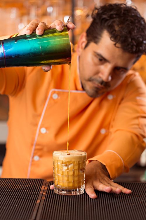 Free Bartender pouring a cocktail with precision in a vibrant bar setting. Stock Photo