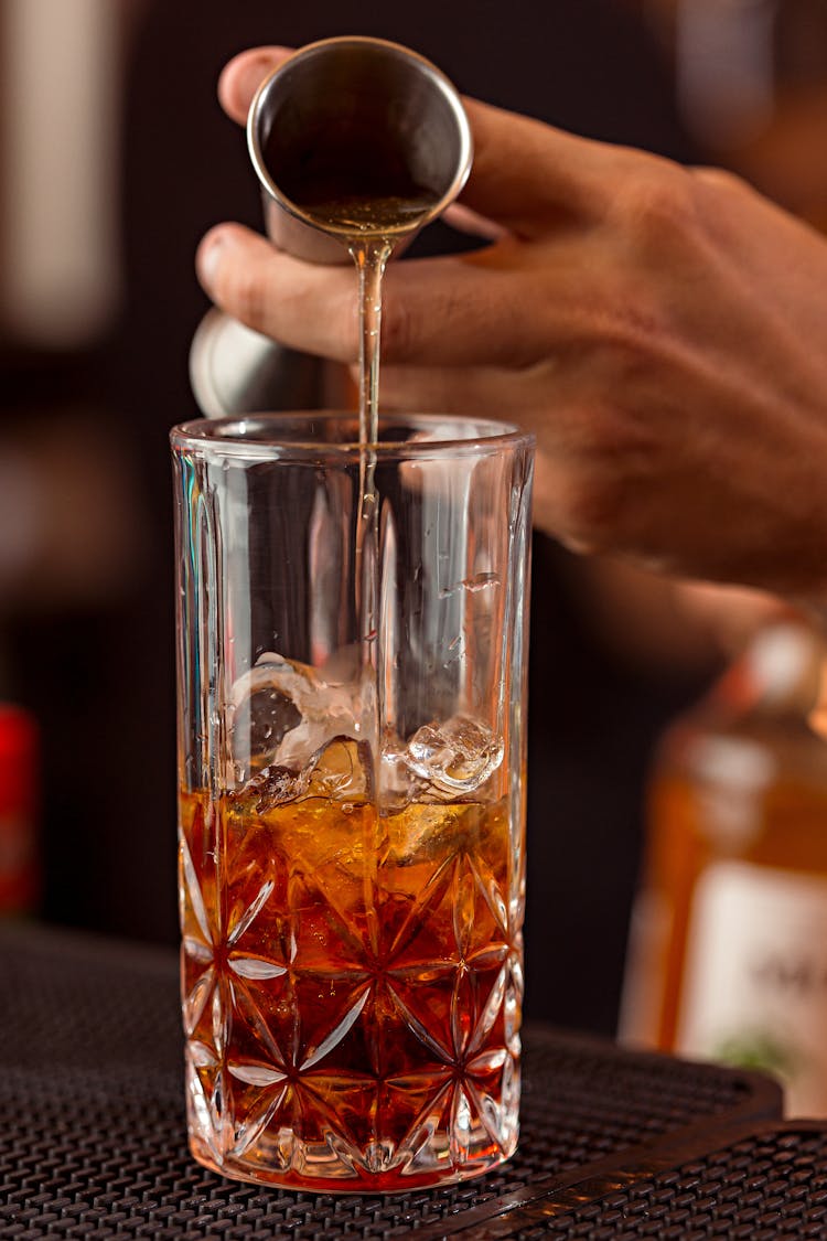 Person Pouring Brown Liquid On Clear Drinking Glass