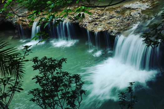 Serene waterfall flowing over rocks, surrounded by lush greenery and nature.